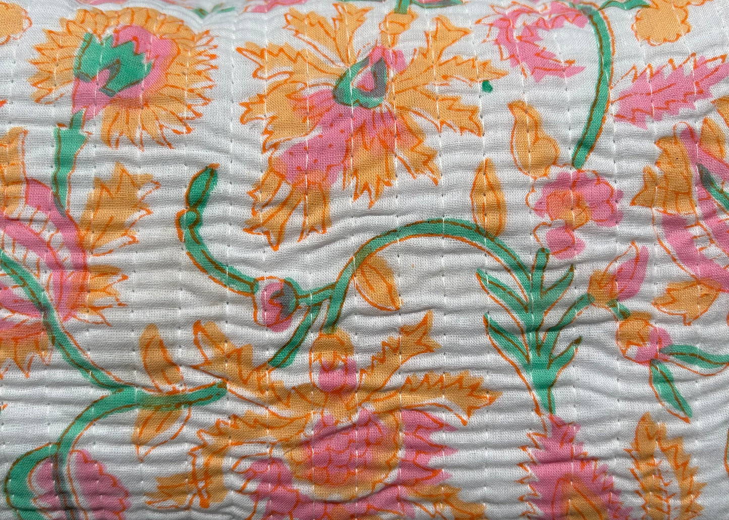 A quilted cotton block printed wash bag with a floral pattern, featuring orange tassels on the zipper.